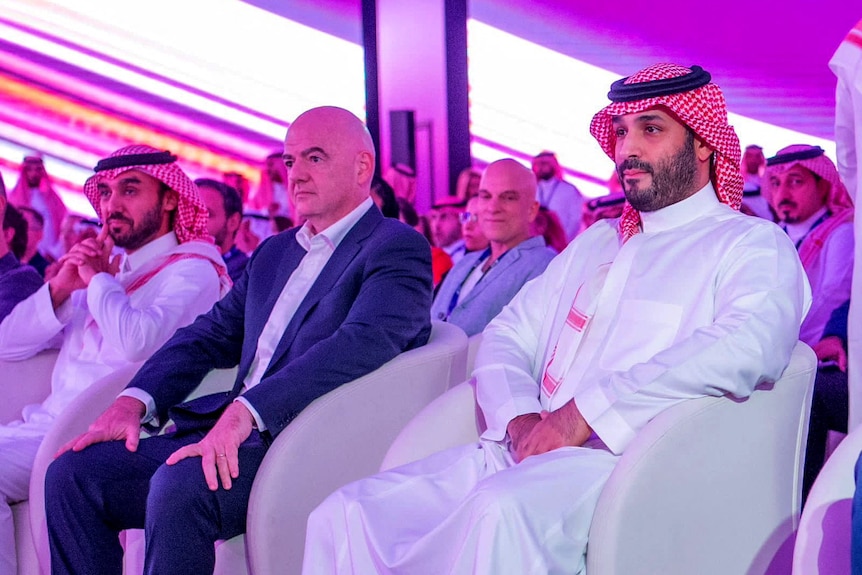 Gianni Infantino in a pink-lit room sitting on white armchairs next to Saudi Crown Prince Mohammed Bin Salman