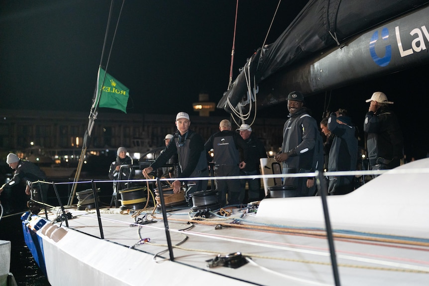 Sailors leaning on railings or standing around on a yacht deck at night.