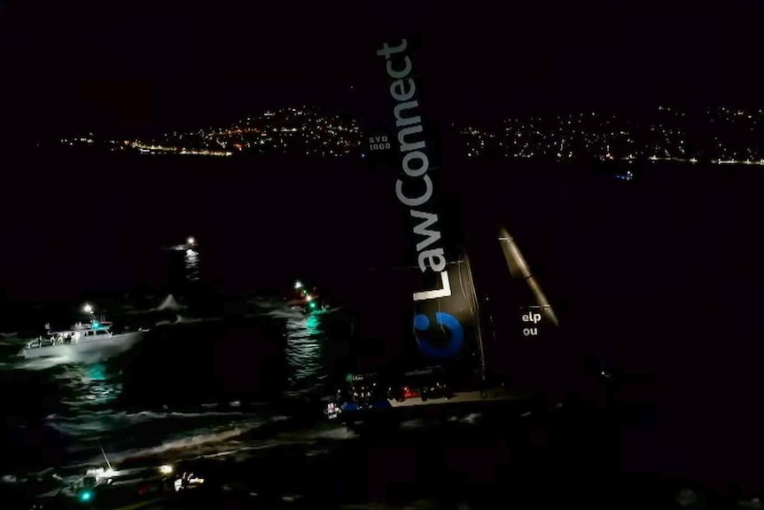 A large yacht with black sails at night.