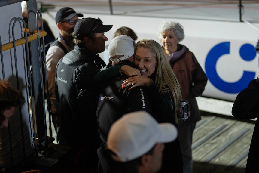 A woman hugs a male sailor at the dock in Hobart as other crew members stand nearby