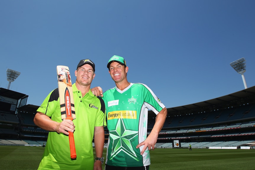 David Warner holds a cricket bat while standing with Shane Warne, in Melbourne Stars kit, at the MCG.