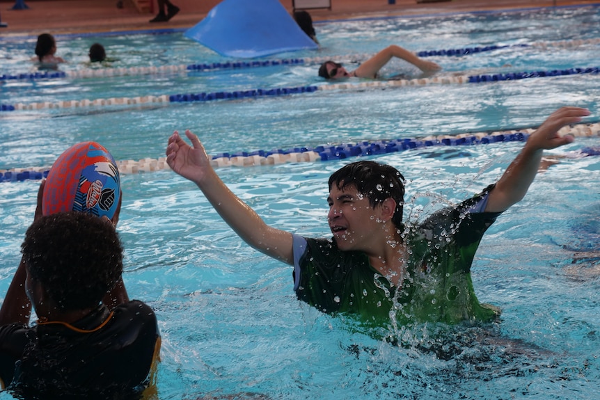 A wide of a child holding a footy and another trying to reach it