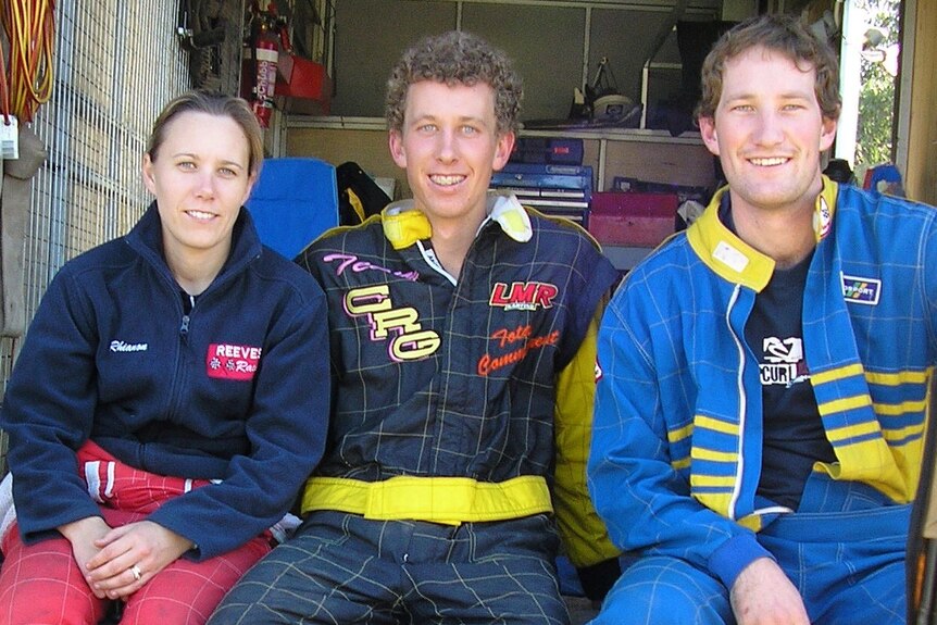 A young woman and two young men wearing sports shirts, sitting together on the back of a truck.