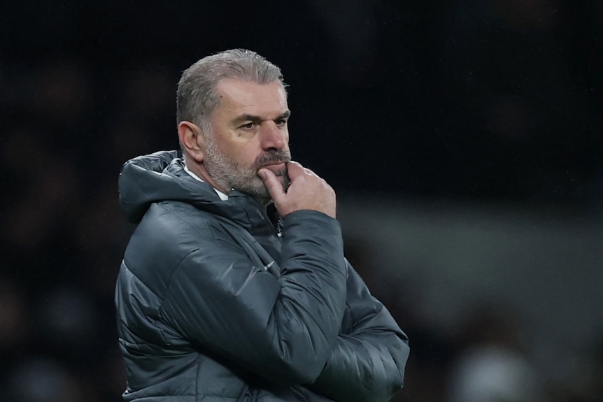 Tottenham Hotspur manager Ange Postecoglou holding his chin. thinking, on a football pitch touchline