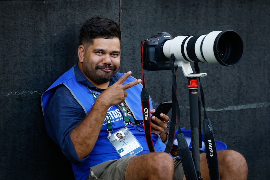 man with large sports camera gestures and smiles towards the photographer