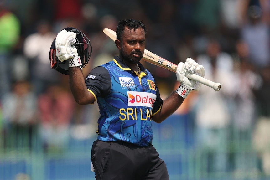 Sri Lanka batter Charith Asalanka holds his helmet and bat up to celebrate during an ODI.