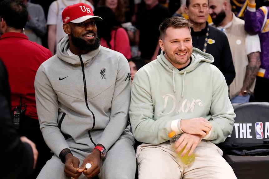 LeBron James and Luka Doncic sitting next to each other on the sideline at a Lakers game.