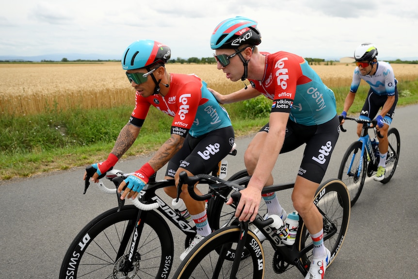 Caleb Ewan rides while teammate Paskal Eenkhoorn puts his hand on his back