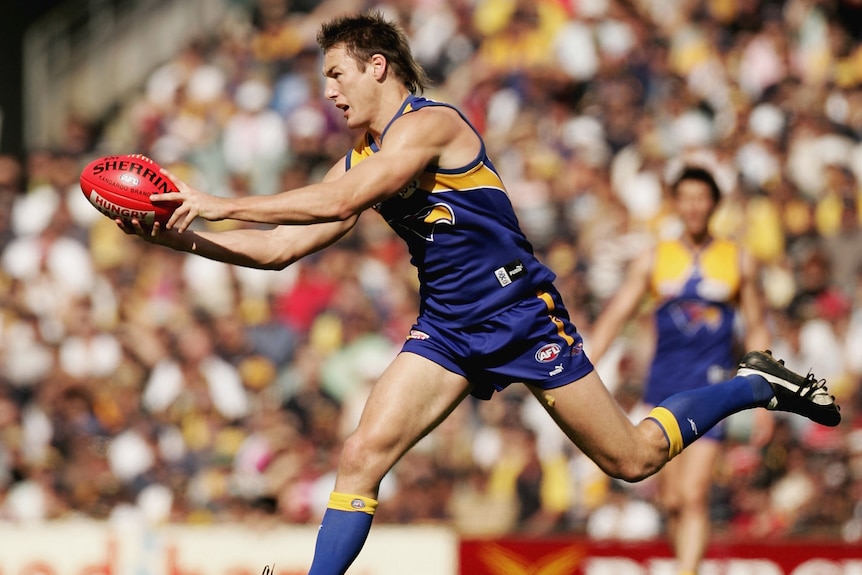 An AFL player stretches to catch the football while playing for the West Coast Eagles.