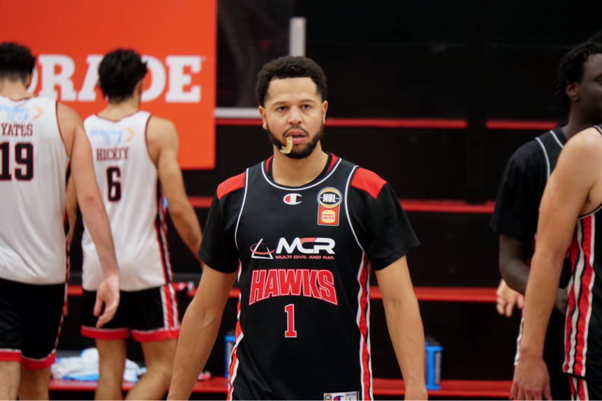 Tyler Harvey walks on the court in team uniform with his mouthguard hanging out of his mouth.