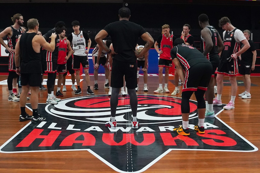 Hawks players gather at the centre of a court and listen to coaching staff.