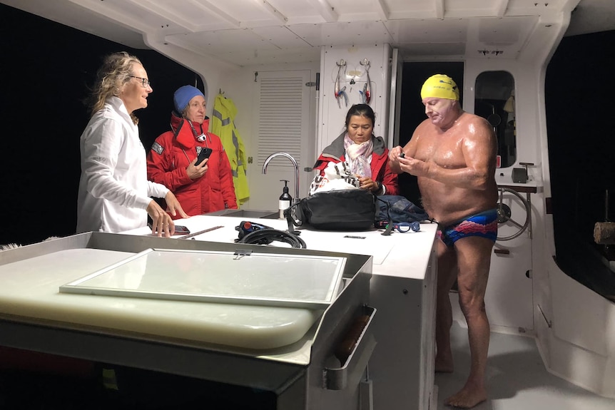 A man in swimmers and a cap on boat with his support crew preparing for a marathon ocean swim