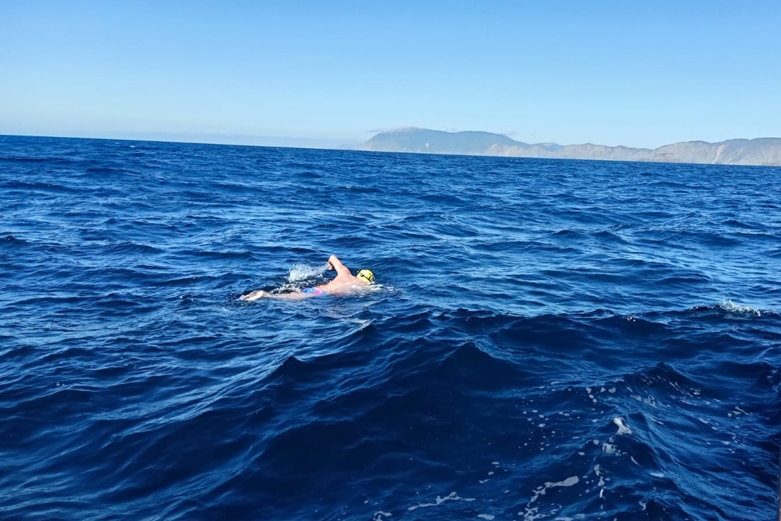 A man wearing a swimming cap and goggles swimming in the ocean next to a boat
