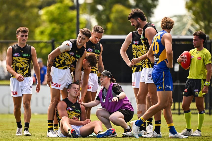 Sam Lalor winces in pain on the ground as a trainer assists him and teammats show concern
