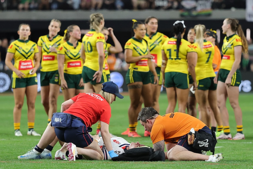 Vicky Whitfield lies on her back with medical staff around her and the Australia team looking on