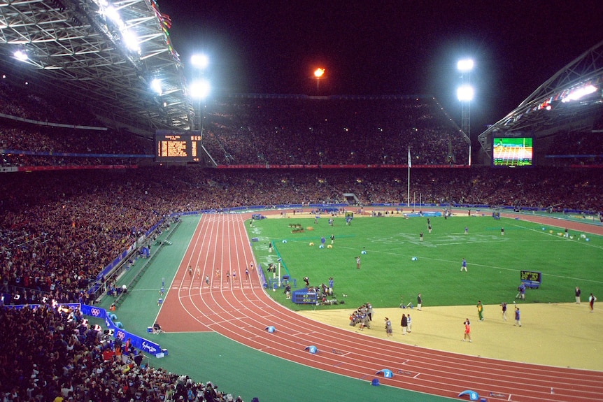 Packed stadium at night has floodlights illuminating the track and field below