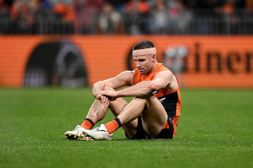 Jesse Hogan sitting on the AFL field, looking dejected and exhausted after a loss