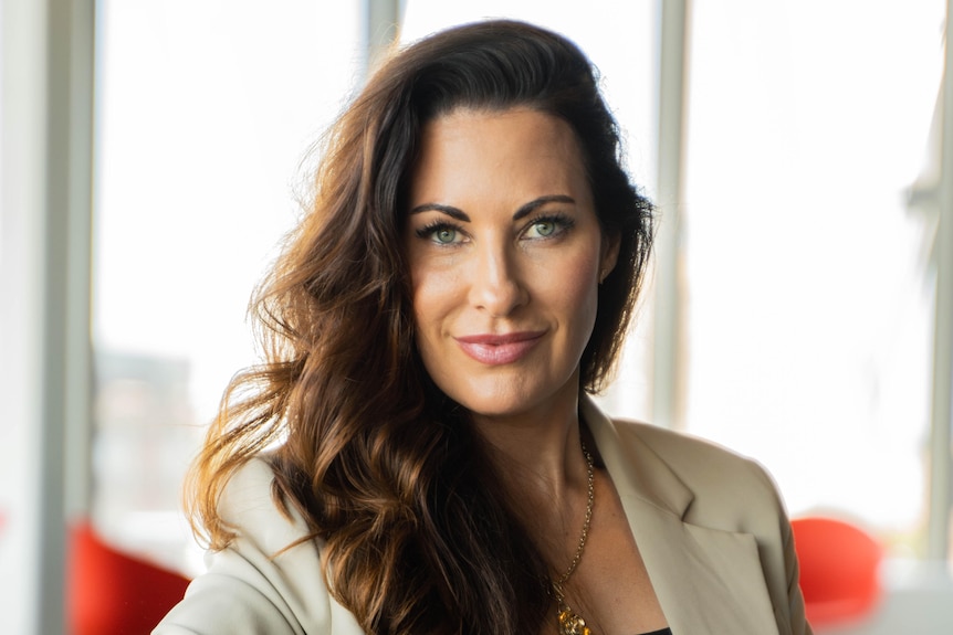 A woman with long brown hair wears a cream suit jacket and blue smart watch.