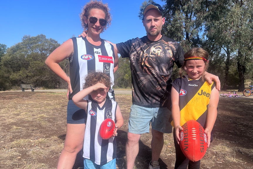 Two parents with their two kids who are each holding an AFL ball. 