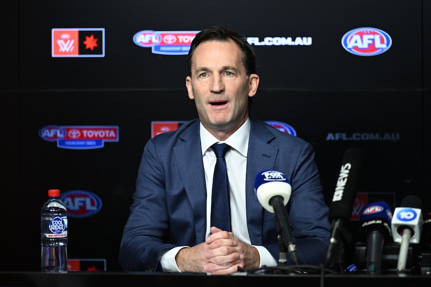 A top AFL executive sits at a desk facing the media with microphones in front of him.