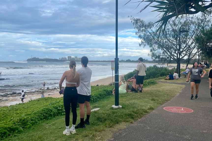 A lady stands wearing lycra and looks out to the ocean off Mooloolaba Beach.