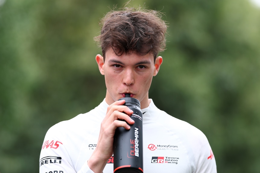 Oliver Bearman walking through the F1 paddock, drinking from a bottle