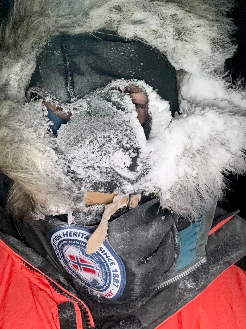 A man in a parka and mask covered in ice.