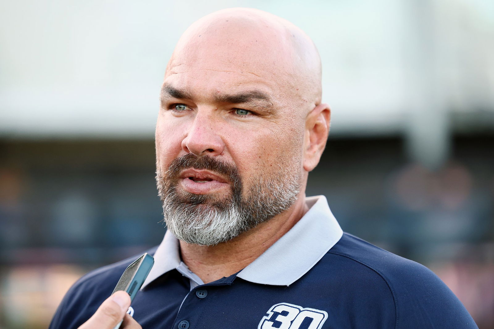 A bald man with a beard looks slightly off caera.