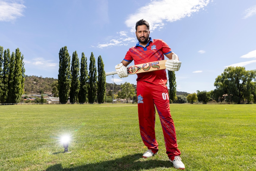 A man holding a cricket bat, standing on a green cricket pitch.