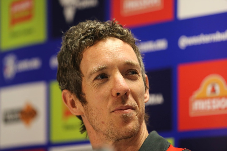 A close-up shot of a white man's face, with dark hair and a slight smile.