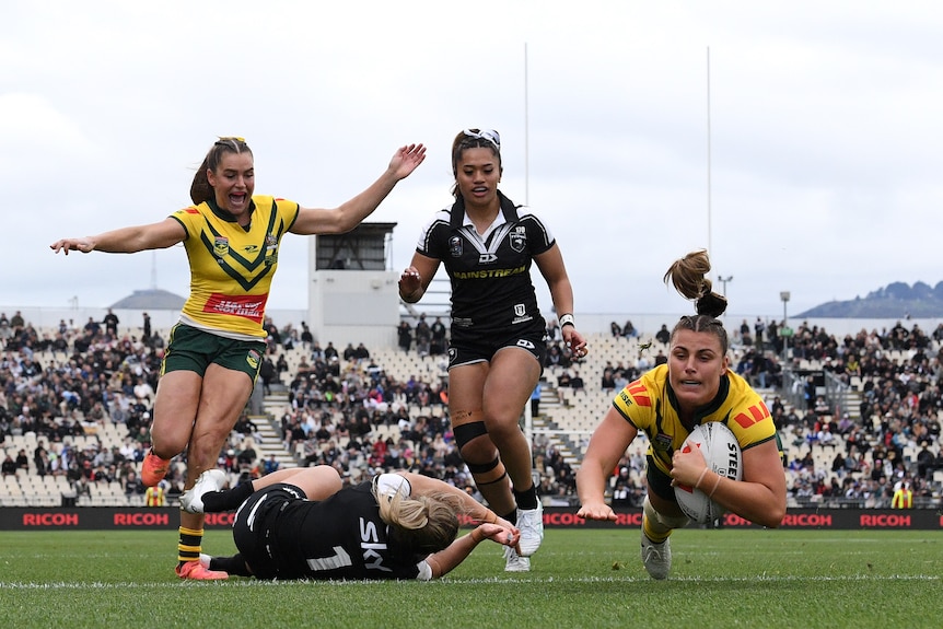 An Australian rugby player dives over to score a try for her team as New Zealand defenders try in vain to stop her.
