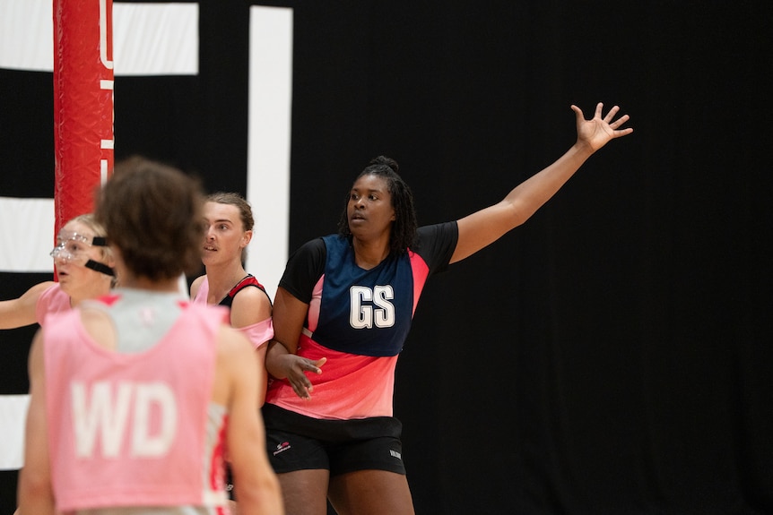 Romelda holds one arm up high attempting to block a goal while body blocking two opponents