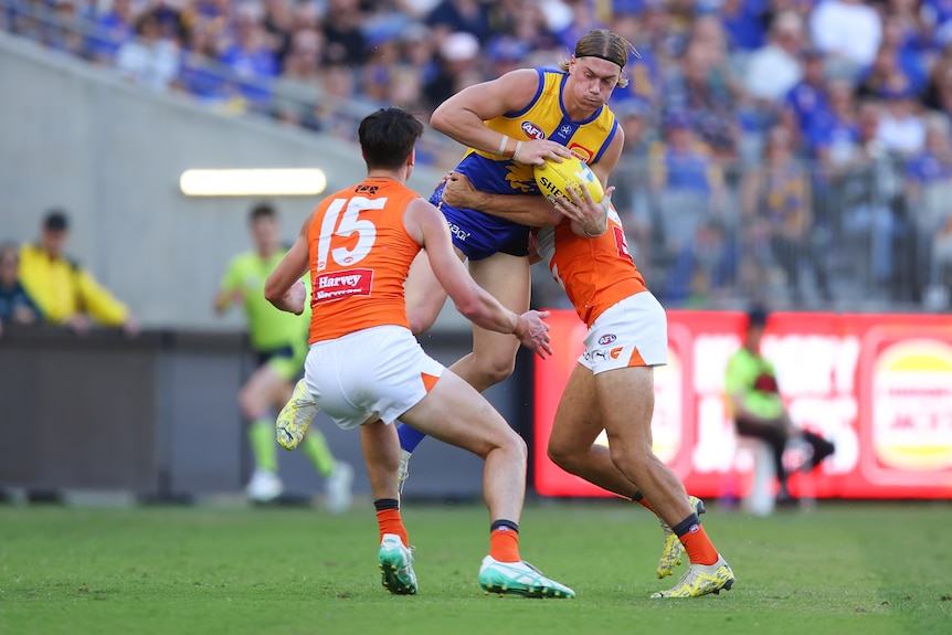Harley Reid is tackled mid-air by two GWS Giants players