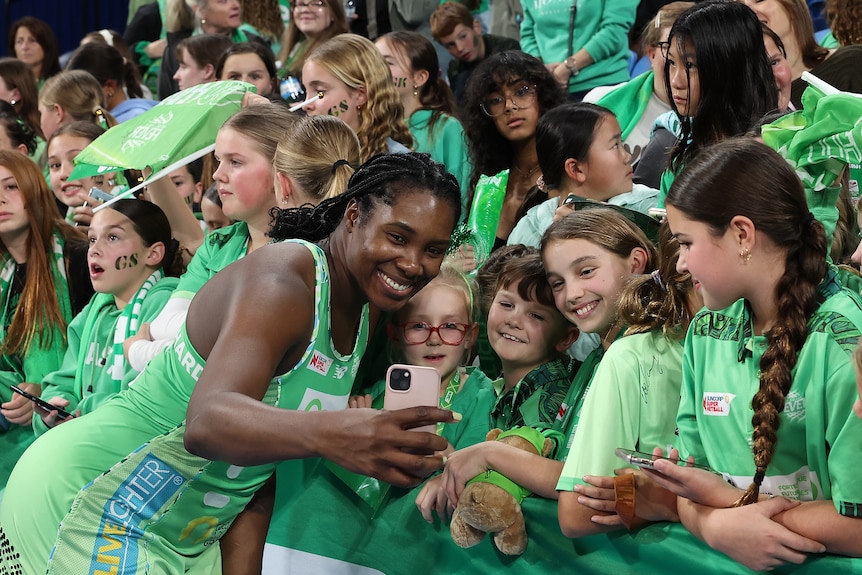 A netballer holds a phone to take a selfie with fans