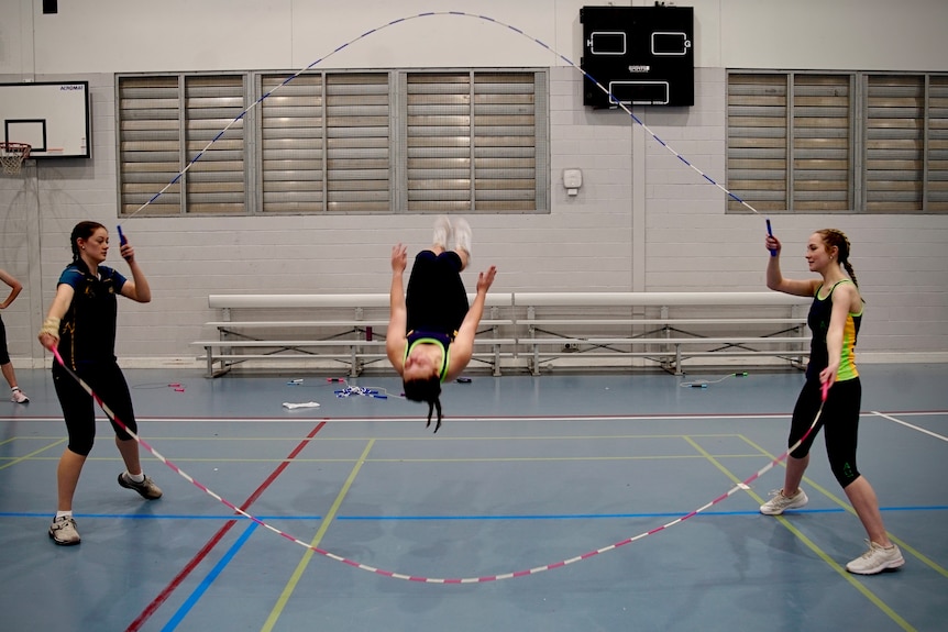 Three young women performing a double dutch jump rope routine which includes a backflip.