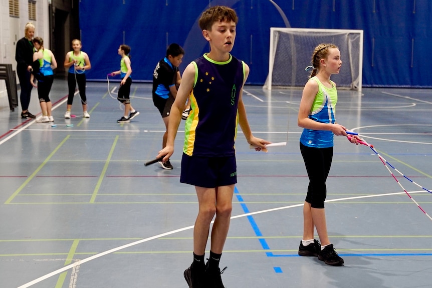 A young boy and girl in activewear jump rope side by side in a gym.