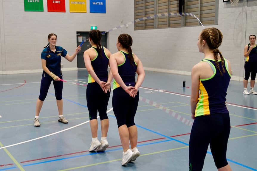 Two young women in activewear stand holding two jump ropes while two others jump within it.