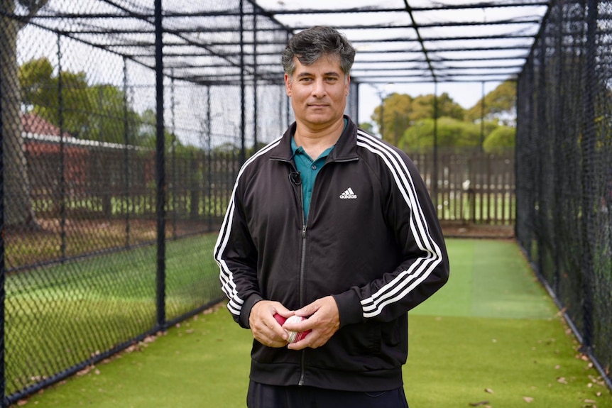 Rene Ferdinands holds a cricket ball while standing in front of cricket training nets