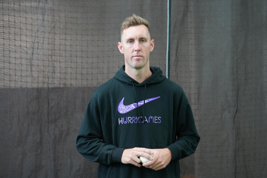 Billy Stanlake wears a black jumper and holds a white cricket ball in both hands