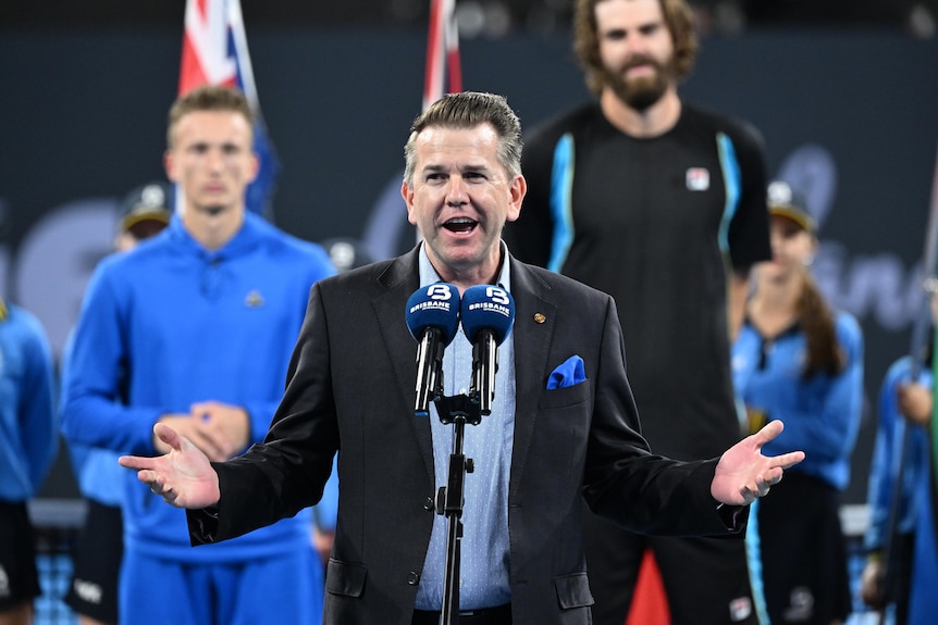 A politician speaking into microphones at an international tennis event.