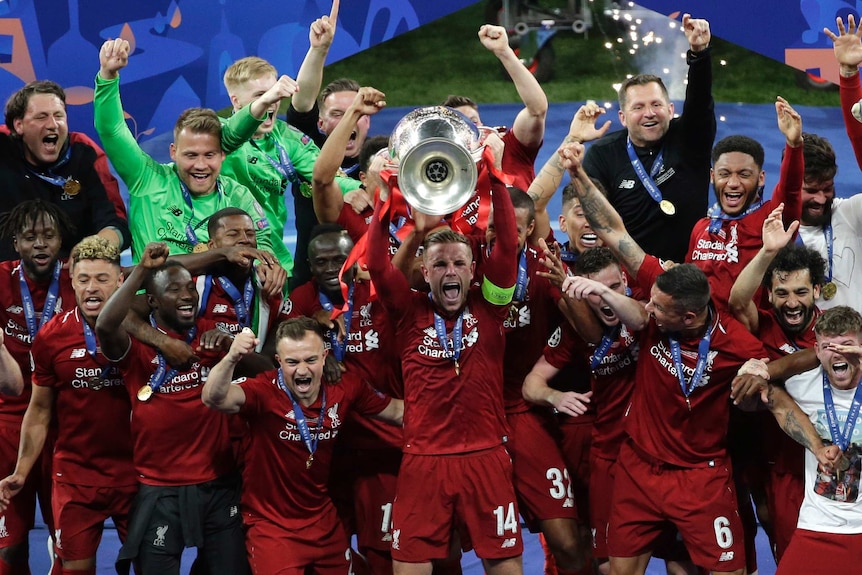 Liverpool's Jordan Henderson lifts a trophy with his team mates cheering in the background