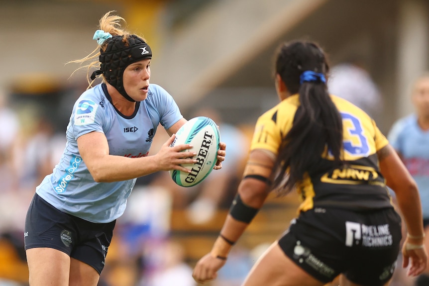 Two rugby players, one in blue and one in yellow, tussle for the rugby ball.