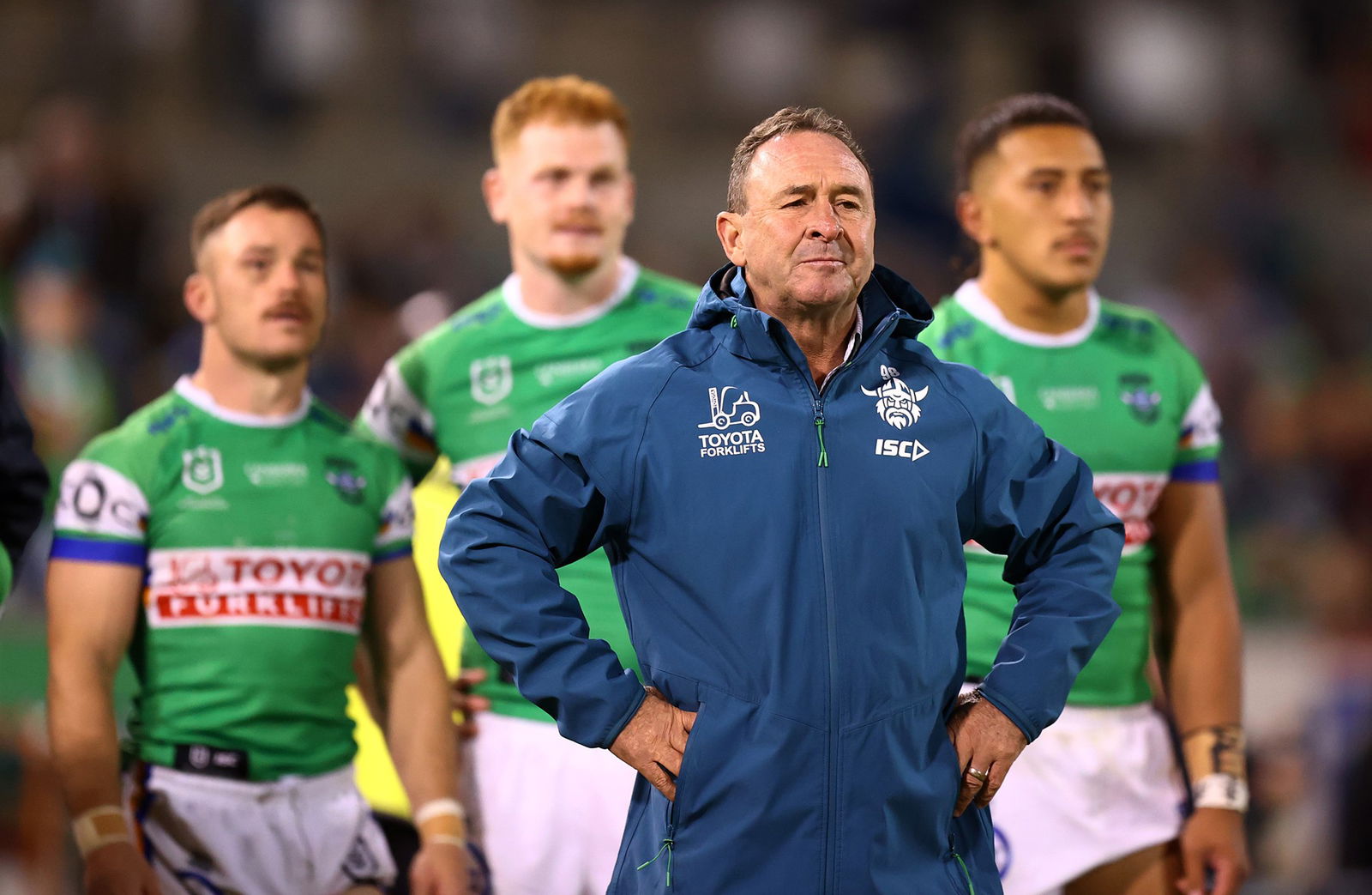 Canberra Raiders coach Ricky Stuart stands in front of Raiders players on the sideline of an NRL match.