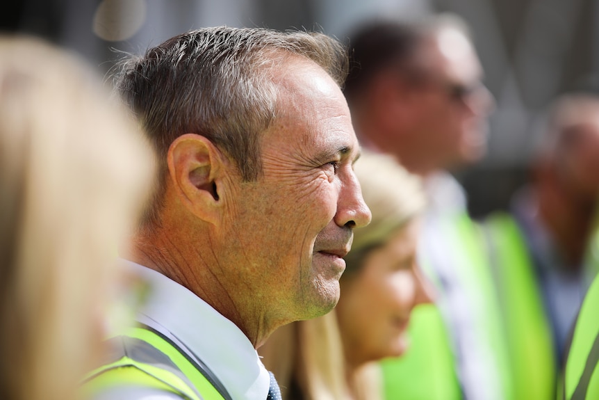 A close-up side-on shot of WA Premier Roger Cook wearing a high-vis vest among other people, whose images are blurred.
