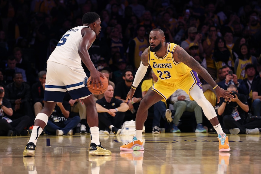 Anthony Edwards holds basketball in right hand while LeBron James defends
