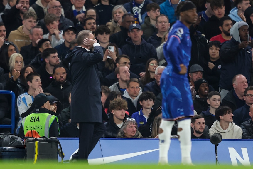 Ange Postecoglou cups his right ear during a Premier League match.