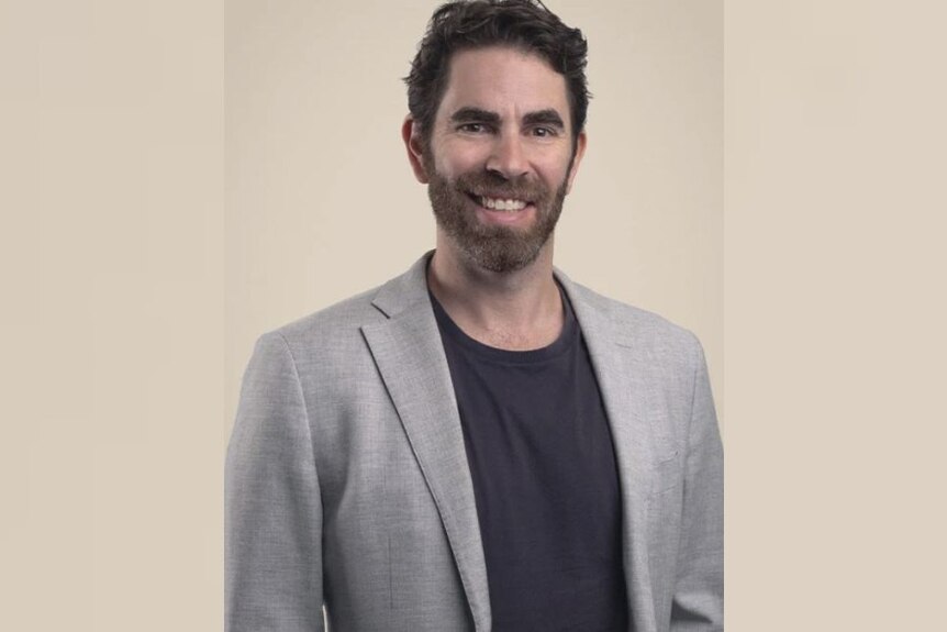 A man named Jarrod Hill in a cream-coloured jacket with a dark shirt. 