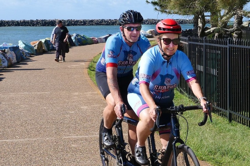 A couple ride tandem on the breakwall footpath wearing their blue team lycra tops.