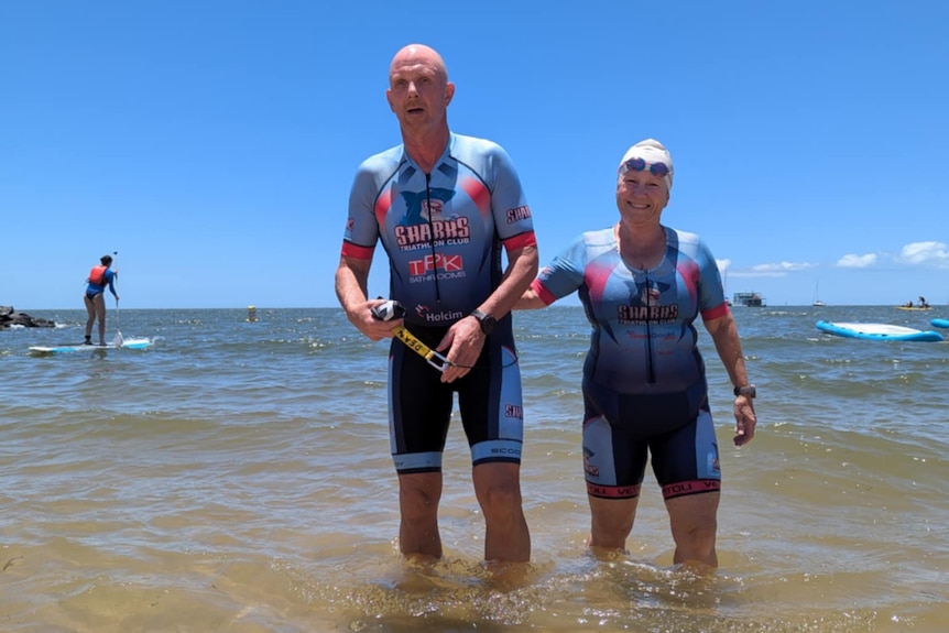 Two older people in full lycra swimsuits standing in the water at river.