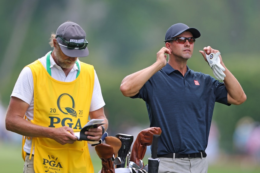 Adam Scott of Australia looks on while his caddy consults a note book